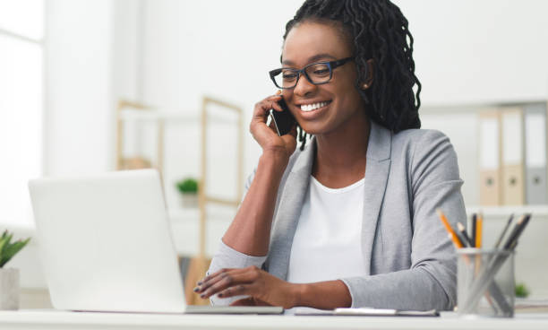 glückliches business-mädchen mit telefon-gespräch mit laptop im büro - business woman stock-fotos und bilder