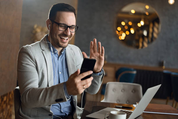 Happy businessman making a video call over smart phone and waving to someone stock photo