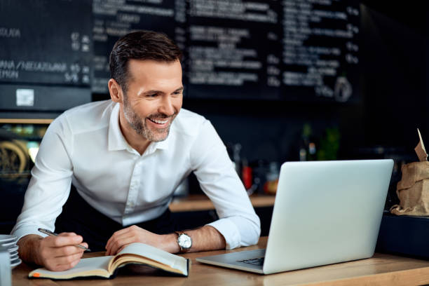 Happy cafe restaurant owner using laptop writing expenses. Small business concept. stock photo