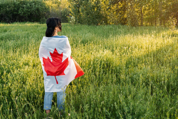 Photo of Happy Canada Day Celebration concept. Brunette woman holding Canadian flag on the back on nature background. Back view