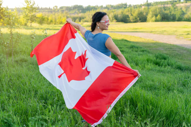 Happy Canada Day Celebration concept. Brunette woman with Canadian flag and themed sunglasses on nature background stock photo