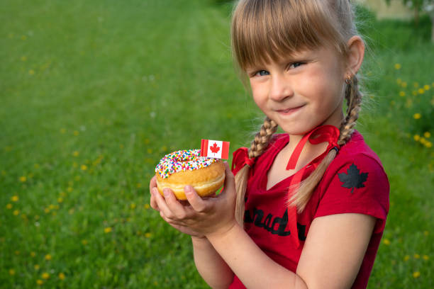 Happy Canada Day Celebration Concept. Smiling girl is holding a sprinkled donut with Canadian flag. Young Canadian Kid stock photo