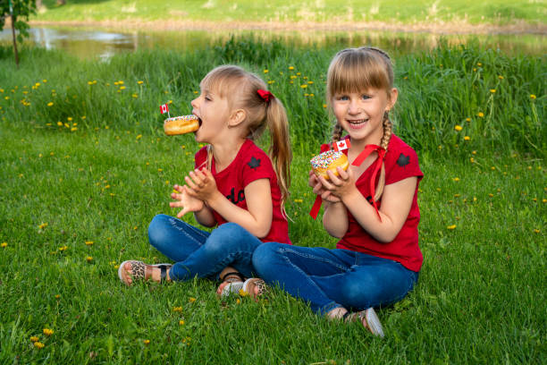 Happy Canada Day Celebration Concept. Two caucasian girls with donuts celebrating outside Canadian Anniverasy stock photo