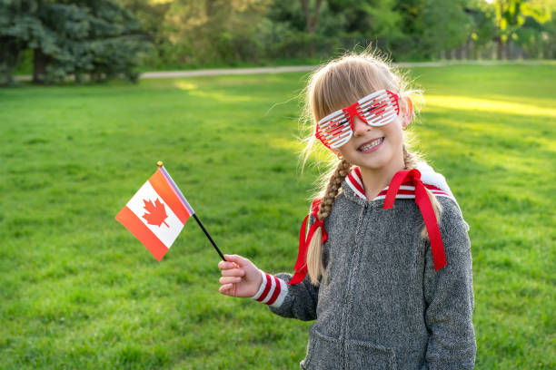 Happy Canda Day Celebrtation concept. Young cute female child with Canadian flag and themed sunglasses in a park stock photo