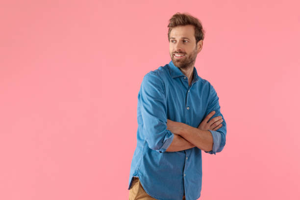 happy casual man looking to side and crossing arms happy casual man looking to side and crossing arms, standing on pink background human limb photos stock pictures, royalty-free photos & images