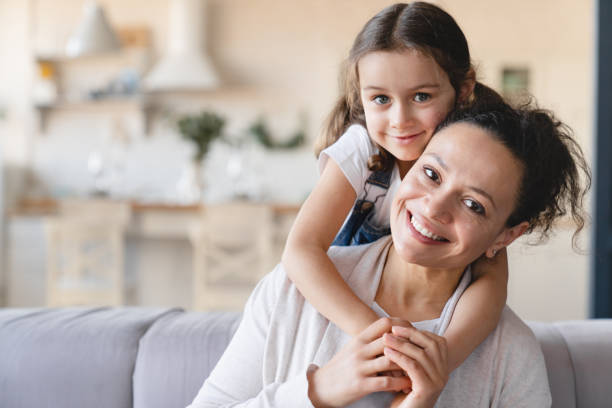 Happy caucasian mother and cute little daughter girl hugging embracing , spending time together looking at camera at home. Love and care, family moments, parenthood and motherhood concept stock photo