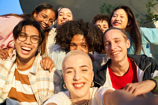 Happy centennial taking smiling selfie. Group of multiethnic students together at campus university. The focus is on the people in the background. High quality photo