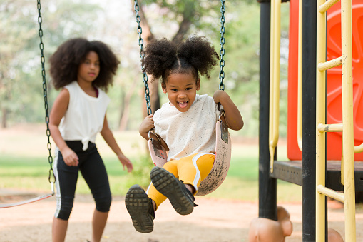 Happy cheerful African American child girl playing on swing at playground in park. Smiling girl having fun on a swing
