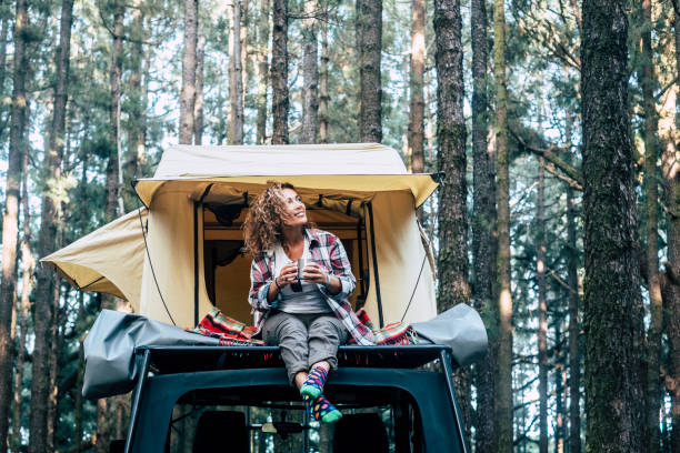 glada glada vackra människor kaukasiska vuxen kvinna sitta ner på taket av bilen med tält i bakgrunden och skogen runt-begreppet resor och njuta av naturen - camping tent bildbanksfoton och bilder