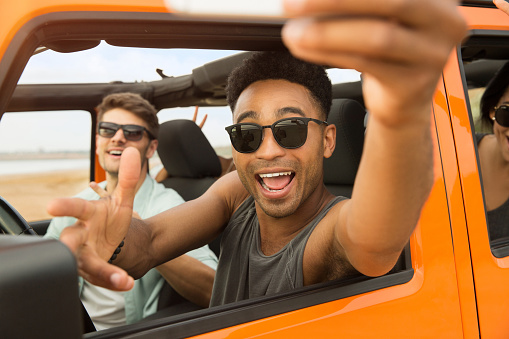 Happy cheerful friends taking a selfie while sitting in a convertible car outdoors