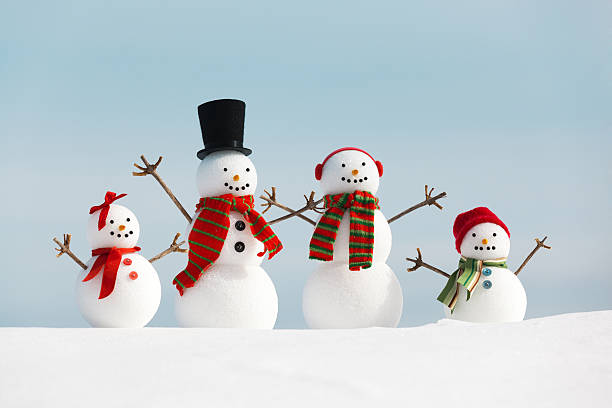 Happy, cheerful snowman family standing in snow, enjoying Christmas winter holiday vacation outdoor fun. Humorous parents and children smile with stick arms raised in delight. Wearing top hat, earmuffs, and scarfs, the cute toy father, mother, boy and girl offspring group together under polar cold blue sky with copy space.