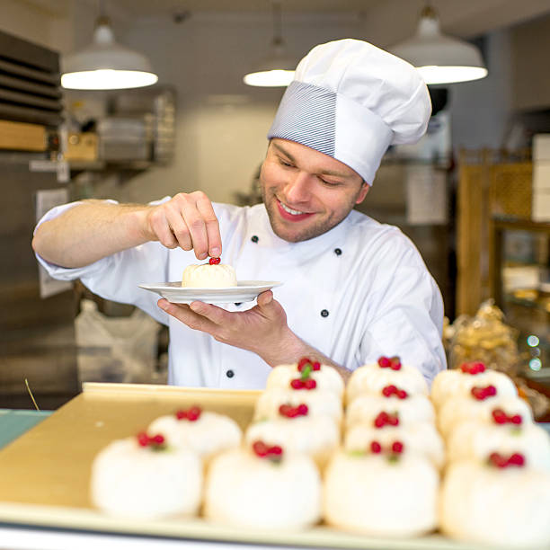 Happy chef creating deserts while garnishing the top Handsome confectioner in uniform decorating cakes in the pastry shop confectioner stock pictures, royalty-free photos & images