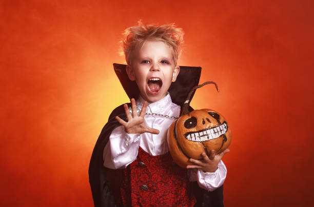 niño niño feliz en trajes de vampiro en el fondo rojo oscuro en halloween - halloween vampire fotografías e imágenes de stock