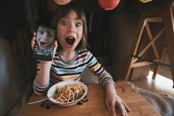 Happy child eating spaghetti and taking selfie at in a self made house tent stock photo