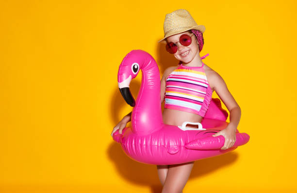 happy child girl in swimsuit with swimming ring flamingo on colored yellow background happy child girl in swimsuit with swimming ring flamingo on a colored yellow background little girls in bathing suits stock pictures, royalty-free photos & images