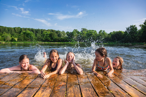 Happy little girls having fun playing in a lake splashing water during summer holidays