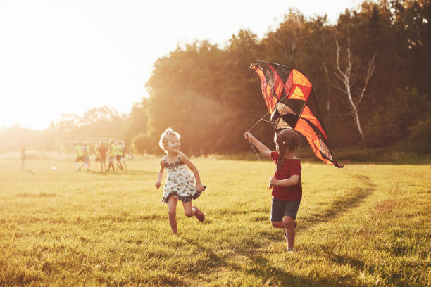 gelukkige kinderen lanceren een vlieger in het veld bij zonsondergang. kleine jongen en meisje op de zomervakantie - beschermd natuurgebied stockfoto's en -beelden