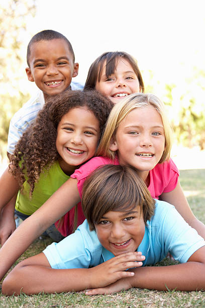 5 happy children of different races piled up in park Group Of Children Piled Up In Park smiling at camera  children only stock pictures, royalty-free photos & images