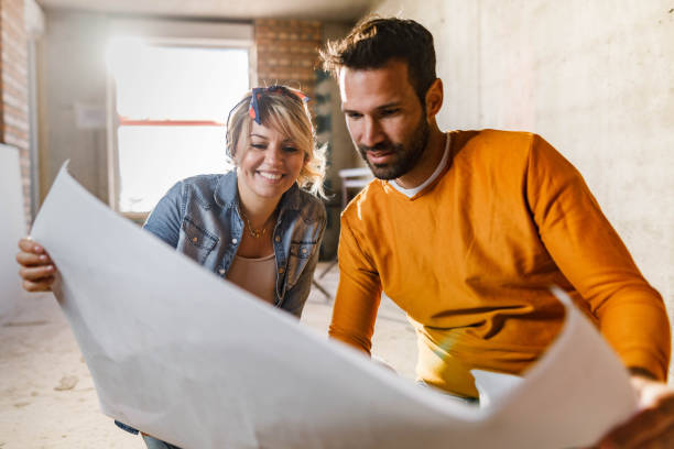 Happy couple analyzing plans at their renovating apartment. stock photo