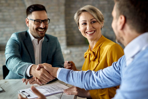 Happy couple came to an agreement with insurance agent in the office. Happy woman signing a contract while her husband is handshaking with real estate agent in the office. 3 business deal shakehands stock pictures, royalty-free photos & images