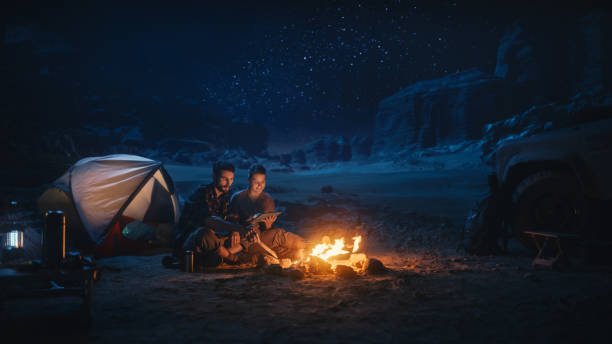 Happy Couple Camping in the Canyon at Night, Use Digital Tablet Computer, Sitting by Campfire. Two people Have Fun, Smile, Post Traveling Photos on Social Media, Watch Funny Videos on Internet Happy Couple Camping in the Canyon at Night, Use Digital Tablet Computer, Sitting by Campfire. Two people Have Fun, Smile, Post Traveling Photos on Social Media, Watch Funny Videos on Internet streaming service stock pictures, royalty-free photos & images