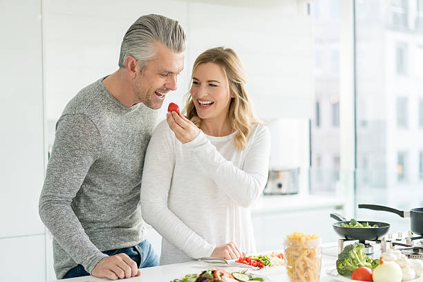 Happy couple cooking at home Happy couple cooking together at home and looking very playful - healthy eating concepts healthy food stock pictures, royalty-free photos & images