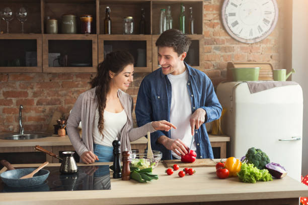 Happy couple cooking dinner together Happy couple cooking dinner together in their loft kitchen at home. Man preparing vegetable salad for his girlfriend, copy space healthy dinner stock pictures, royalty-free photos & images