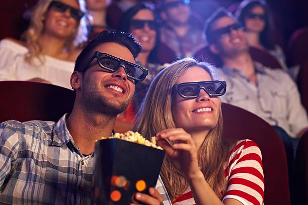 Happy couple in 3D movie Happy couple sitting in movie theater, watching 3D movie, eating popcorn, smiling.. 3 d glasses stock pictures, royalty-free photos & images