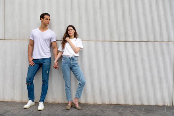 Happy Couple Leaning Against Wall Holding Hands wearing casual clothes in a bright day stock photo