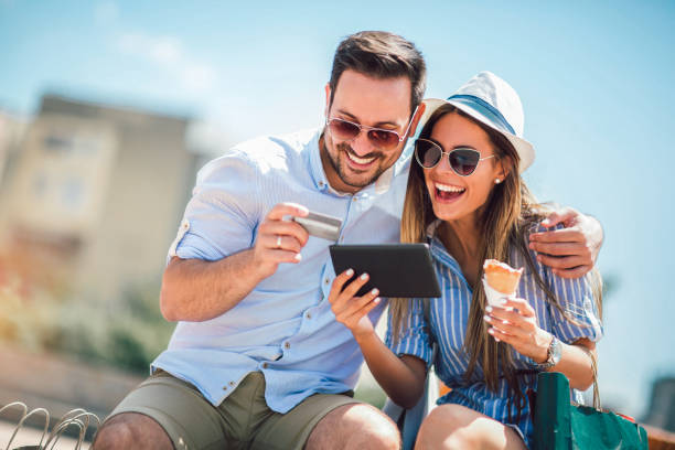 Happy couple paying on line with credit card and digital tablet on the street Happy couple paying on line with credit card and digital tablet on the street credit card purchase photos stock pictures, royalty-free photos & images