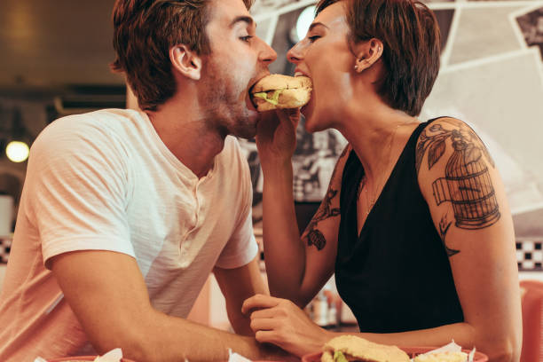gelukkige paar delen een hamburger in een restaurant - romantiek begrippen stockfoto's en -beelden