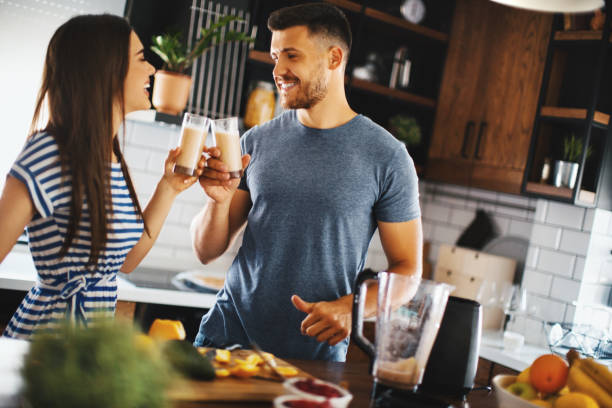 Happy couple toasting with juices in the kitchen. Young couple making healthy drink in their kitchen. They are smiling and toasting with juices. drinking smoothie stock pictures, royalty-free photos & images