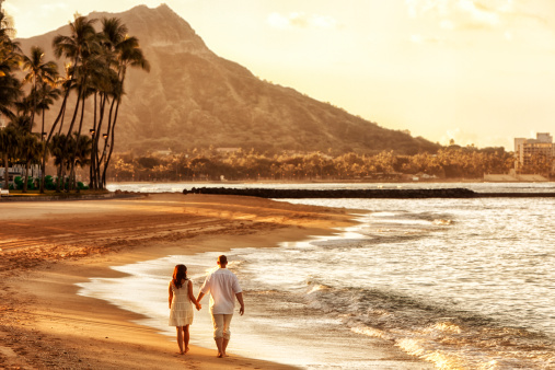 Photo of a happy young couple walking hand-in-hand on Waikiki beach at sunrise.