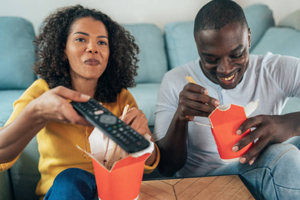 couples heureux regardant la tv - african america man eating chinese food photos et images de collection