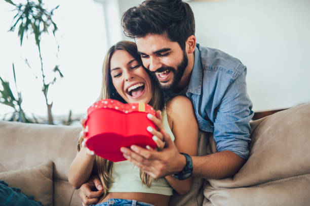 happy couple met geschenk doos knuffelen thuis. - valentines day stockfoto's en -beelden