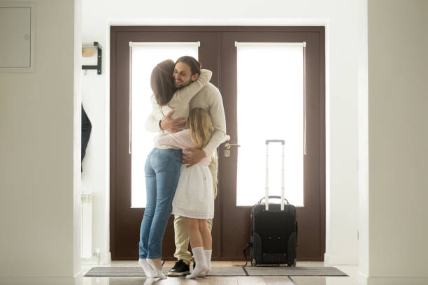 Happy dad hugging family arriving home, welcome home father concept Happy dad hugging family tight arriving from long business trip with suitcase, smiling loving father embracing wife and daughter standing in house hall, welcome back home daddy and reunion concept worker returning home stock pictures, royalty-free photos & images