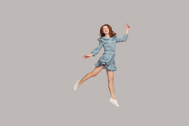 Happy delicate girl in vintage ruffle dress levitating with ballet dance move, hovering in mid-air and smiling joyfully Happy delicate girl in vintage ruffle dress levitating with ballet dance move, hovering in mid-air and smiling joyfully, jumping trampoline, flying up. indoor studio shot isolated on gray background hovering stock pictures, royalty-free photos & images