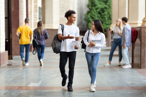 Happy diverse students walking in college campus Happy diverse students walking in college campus during break and talking, copy space students with laptop stock pictures, royalty-free photos & images