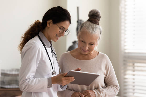 Happy doctor and senior patient use tablet at consultation Happy female doctor and senior patient look at tablet screen discuss treatment or therapy on gadget. Smiling woman nurse and mature client use pad device discussing results in modern hospital. patient stock pictures, royalty-free photos & images