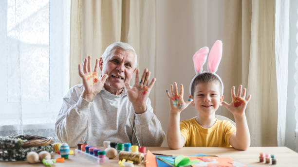 Happy elderly man granfather preparing for Easter with grandson. Portrait of smiling boy with bunny ears painted  colored eggs for Easter stock photo