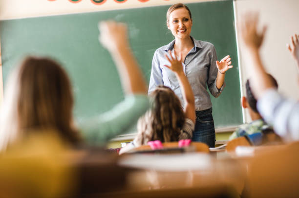 Happy elementary teacher asked a question on a class at school. Happy female teacher asked a question during a class at elementary school. elementary school building stock pictures, royalty-free photos & images