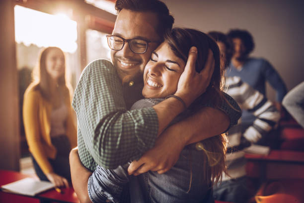 Happy embraced college couple in the classroom. Happy college couple embracing with great affection on a class at lecture hall. embracing stock pictures, royalty-free photos & images