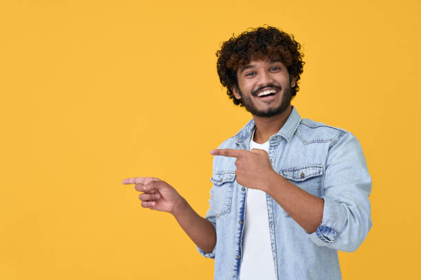 Happy excited young indian man pointing on yellow background. stock photo