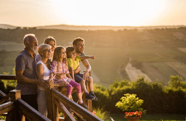 Happy extended family enjoying on a terrace at sunset. Happy multi-generation family enjoying on a balcony of their chalet at sunset. Little boy is aiming at distance. Copy space. multi generation family stock pictures, royalty-free photos & images
