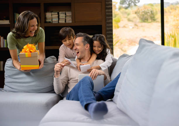 Happy family at home surprising dad for Father's Day Happy Latin American family at home surprising dad with a gift for Father's Day - lifestyle concepts fathers day stock pictures, royalty-free photos & images