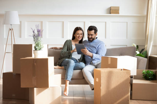 Happy family buying decorations online, moving day concept. Full length happy family sitting on couch among cardboard boxes in new house, using digital tablet, buying decorations online. Smiling couple enjoying moving in new apartment, shopping in internet. relocation photos stock pictures, royalty-free photos & images