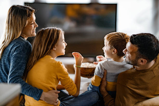 Happy family eating popcorn while watching TV at home. stock photo