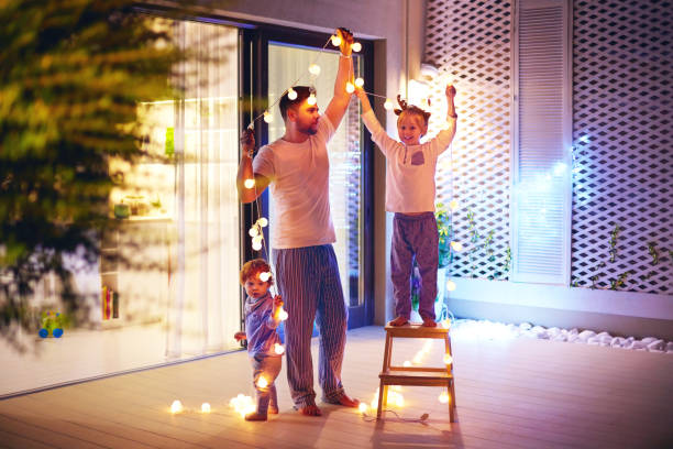 glückliche familie, vater mit söhnen schmücken freifläche terrassenbereich mit girlanden weihnachten - dekorieren stock-fotos und bilder