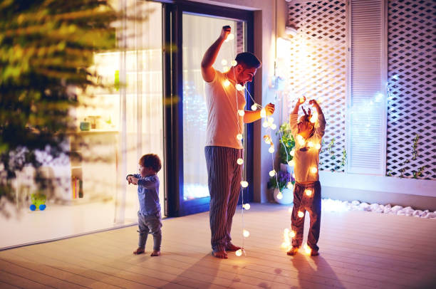 glückliche familie, vater mit söhnen schmücken freifläche terrassenbereich mit girlanden weihnachten - dekorieren stock-fotos und bilder