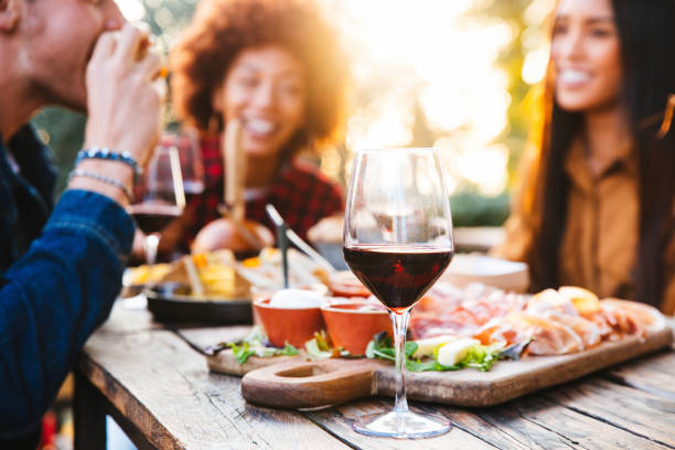 Happy family having barbecue party in backyard - Young friends celebrating at dinner drinking red wine at sunset - Focus on wine glass stock photo